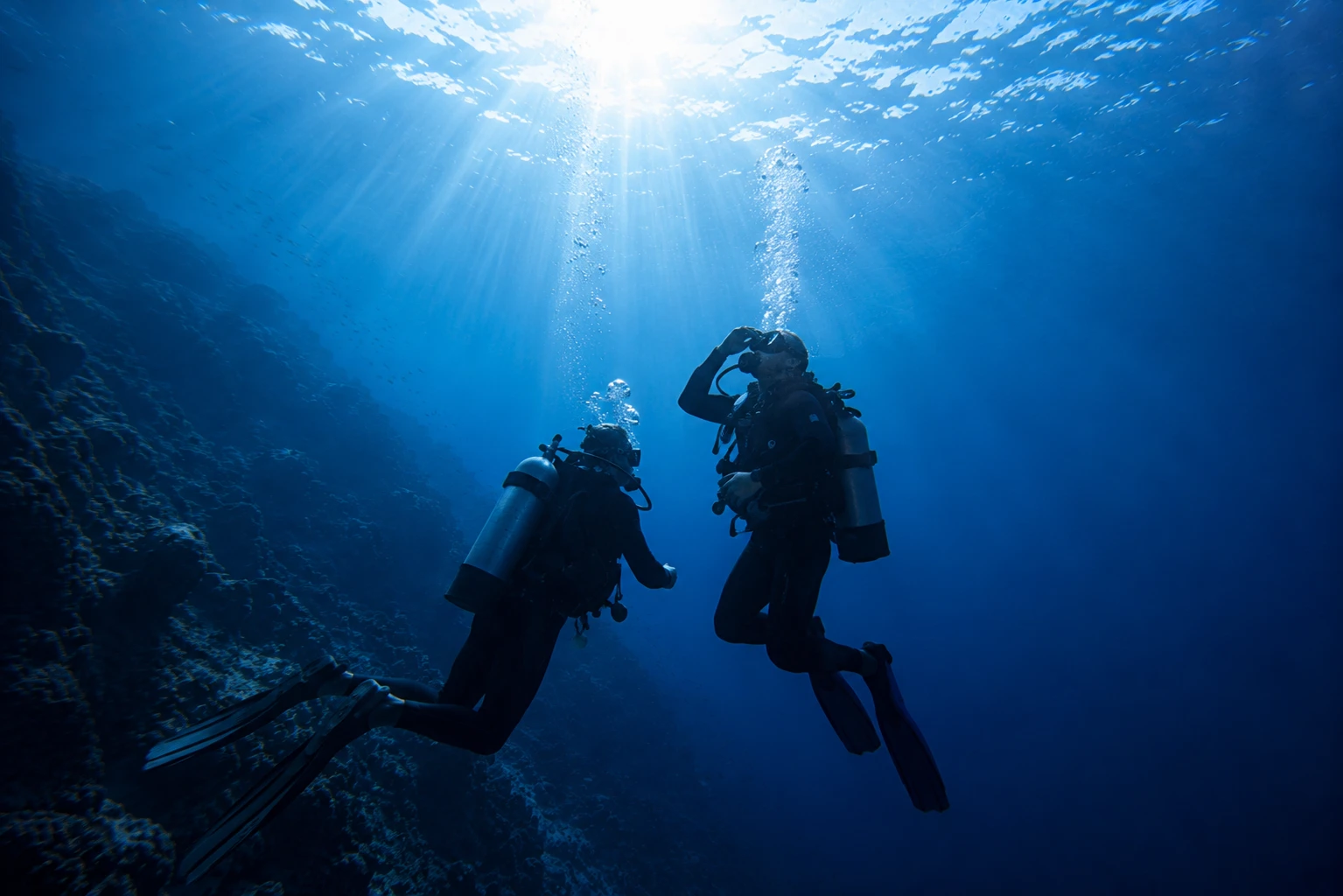 Due subacquei che risalgono lungo una parete rocciosa: corso Open Water Diver