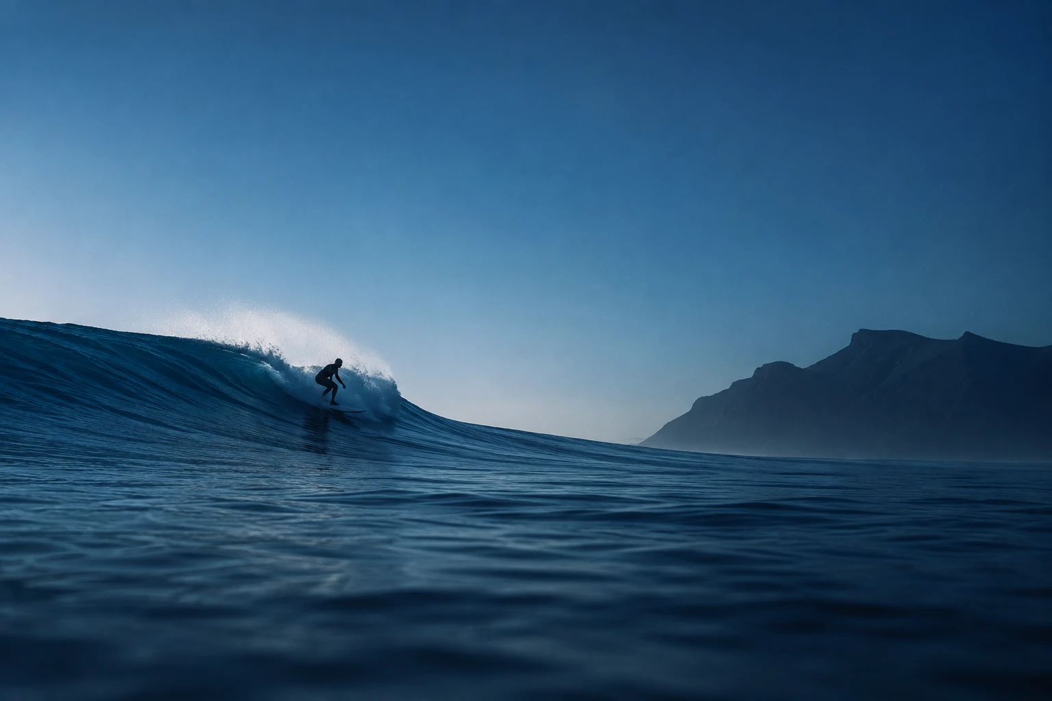 Surfista su un'onda dell'Atlantico, con le montagne di Lanzarote sullo sfondo